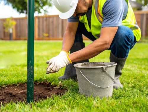 homme en train de réaliser une fixation poteau par scellement béton dans l'herbe 